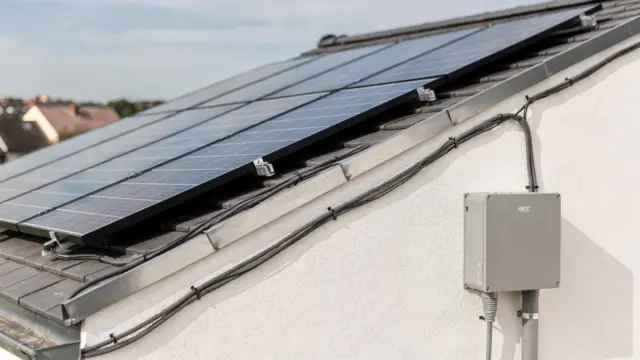 Solarmodule auf einem Hausdach mit Wechselrichter und Kabeln bei der PV-Installation.